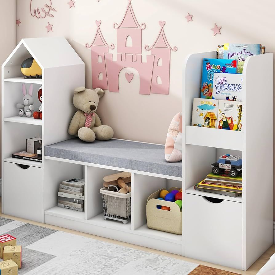 Children’s playroom reading nook with white shelving units, cushioned bench, organized storage for toys and books, decorative pink castle wall art, and alphabet blocks on a patterned rug.